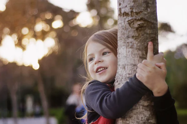 Красивая маленькая девочка улыбается, обнимает ствол дерева. Маленькая девочка — стоковое фото