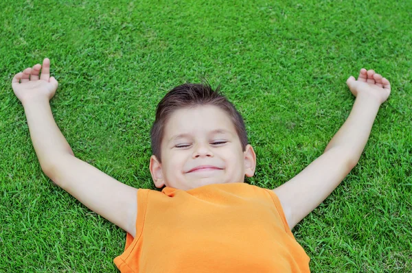 Счастливый маленький мальчик лежит на зеленой траве. Он наслаждается чудом. — стоковое фото
