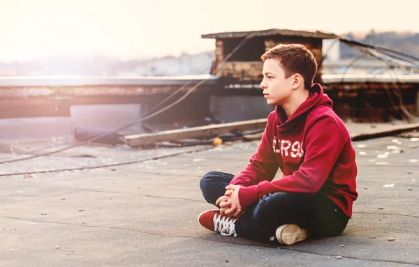 Серьезный подросток сидит на крыше дома — стоковое фото