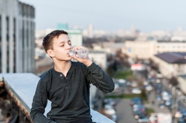 Çatının kenarında oturan genç suyu içer