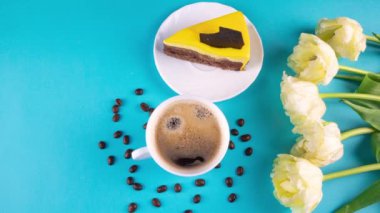 Köpüklü taze espresso kahvesi. Bir fincan kahve, bir buket sarı lale ve açık mavi arka planda fotokopi alanı olan bir dilim pasta. Sevdiğin biri için kahvaltı, 4k