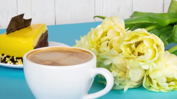 Φρέσκος αρωματικός καφές εσπρέσο με αφρό. Ένα φλιτζάνι καφέ με ένα μπουκέτο κίτρινες τουλίπες και μια φέτα κέικ σε γαλάζιο φόντο με χώρο αντιγραφής. Πρωινό για ένα αγαπημένο πρόσωπο, 4k — Αρχείο Βίντεο