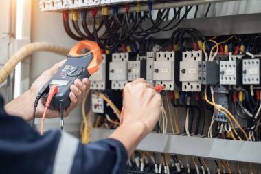 Elektrik mühendisi elektrik kabinesi kontrolündeki voltaj ve elektrik akımını ölçen bir testçi, elektrik sisteminin işleyişini konsept olarak kontrol ediyor .