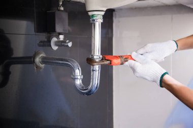 Tesisatçı ayarlanabilir anahtarla beyaz lavabo borusunu tamir ediyor..