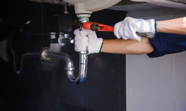 Tesisatçı ayarlanabilir anahtarla beyaz lavabo borusunu tamir ediyor..