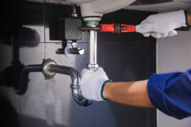 Tesisatçı ayarlanabilir anahtarla beyaz lavabo borusunu tamir ediyor..