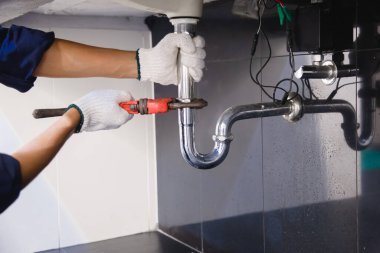 Tesisatçı ayarlanabilir anahtarla beyaz lavabo borusunu tamir ediyor..
