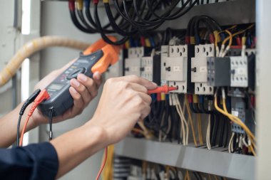 Elektrik mühendisi elektrik kabinesi kontrolündeki voltaj ve elektrik akımını ölçen bir testçi, elektrik sisteminin işleyişini konsept olarak kontrol ediyor .