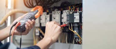 Elektrik mühendisi elektrik kabinesi kontrolündeki voltaj ve elektrik akımını ölçen bir testçi, elektrik sisteminin işleyişini konsept olarak kontrol ediyor .