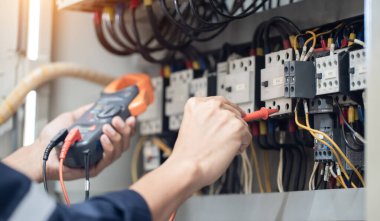 Elektrik mühendisi elektrik kabinesi kontrolündeki voltaj ve elektrik akımını ölçen bir testçi, elektrik sisteminin işleyişini konsept olarak kontrol ediyor .