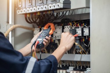 Elektrik mühendisi elektrik kabinesi kontrolündeki voltaj ve elektrik akımını ölçen bir testçi, elektrik sisteminin işleyişini konsept olarak kontrol ediyor .