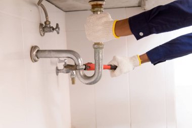 Tesisatçı ayarlanabilir anahtarla beyaz lavabo borusunu tamir ediyor..