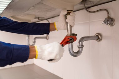 Tesisatçı ayarlanabilir anahtarla beyaz lavabo borusunu tamir ediyor..