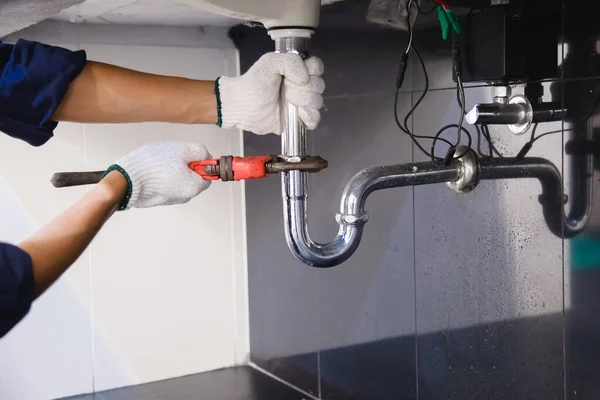 Tesisatçı ayarlanabilir anahtarla beyaz lavabo borusunu tamir ediyor..