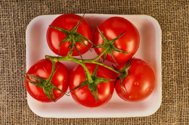 Beyaz plaka ve çuval bezi arka planda ortak şubesi ile kırmızı tatlı domates