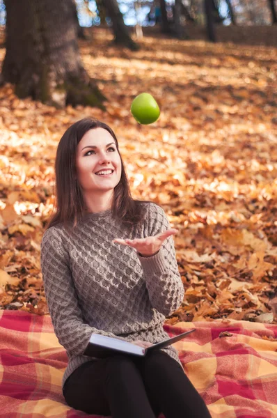 Woman with book and apple sitting on a rug