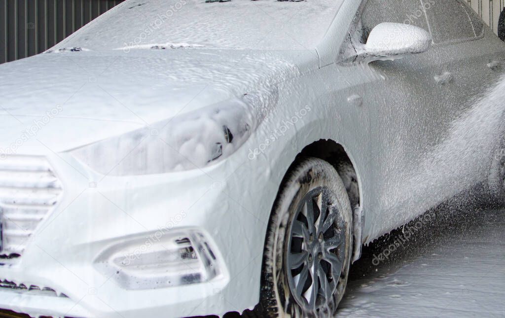 The driver of a car drove into a self-service car wash, using a hose with a spray with high pressure water washes away the remaining foam from the windshield and hood