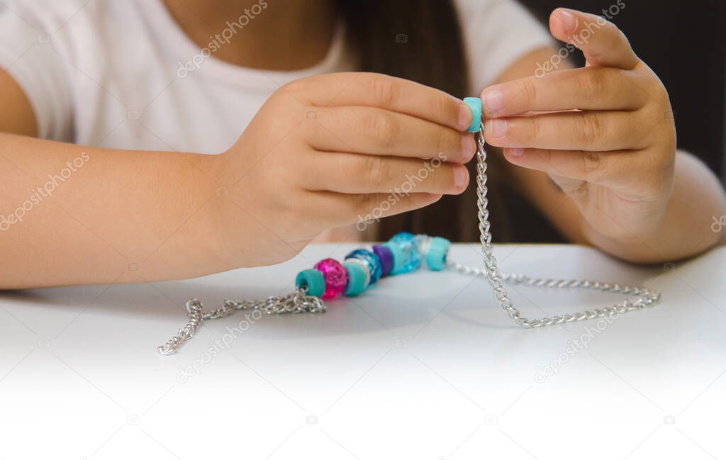 The girl is stringing blue and pink beads from the creativity kit on a chain. Fine motor skills, development of children. Close-up. Blur, concept.