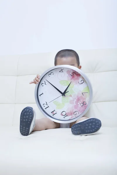 Bonito menino chinês jogando um relógio no sofá — Fotografia de Stock