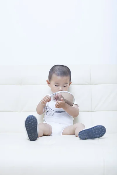 Милый китайский мальчик, играющий в зеркало на диване — стоковое фото