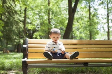 Ormanda bir bankta oynayan sevimli Çinli bebek çocuk
