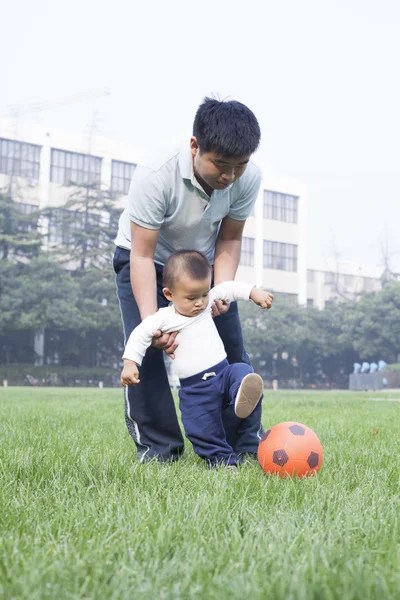 Çince baba ve oğul çayırda futbol oynamak