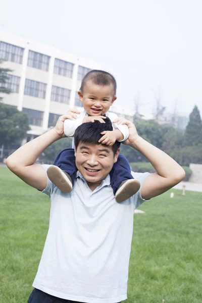Glücklicher chinesischer Vater, der seinen Sohn auf seinen Schultern trägt — Stockfoto