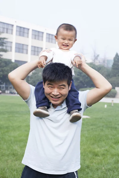Glücklicher chinesischer Vater, der seinen Sohn auf seinen Schultern trägt — Stockfoto