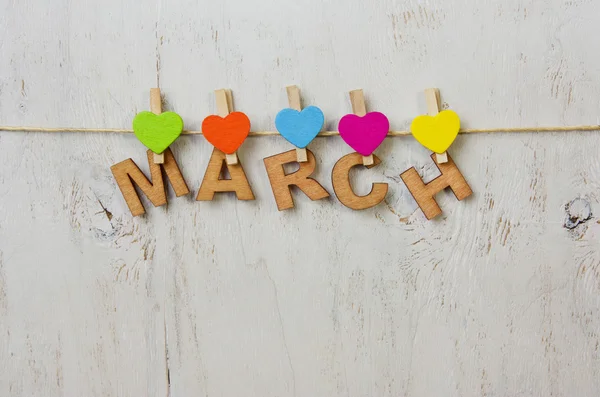 Palavra Março e corações multicoloridos em um fundo branco de madeira — Fotografia de Stock