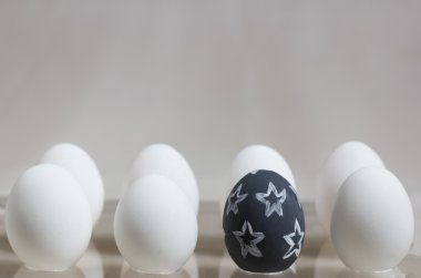 one black egg with a pattern among several white eggs clipart