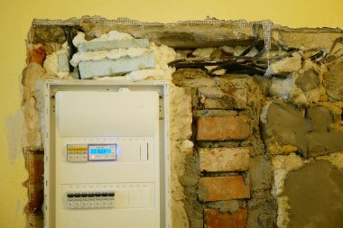 Elektrik dağıtım paneli devre kesici, sigorta kutusu kapatıcısı, kırmızı tuğla ve ölümlü duvar tellerine bağlı güç beslemesini kontrol ediyor. Kalın katmanlar beton, yenilenme ya da yeni kurulum projesinde alçı ya da yeni detay.