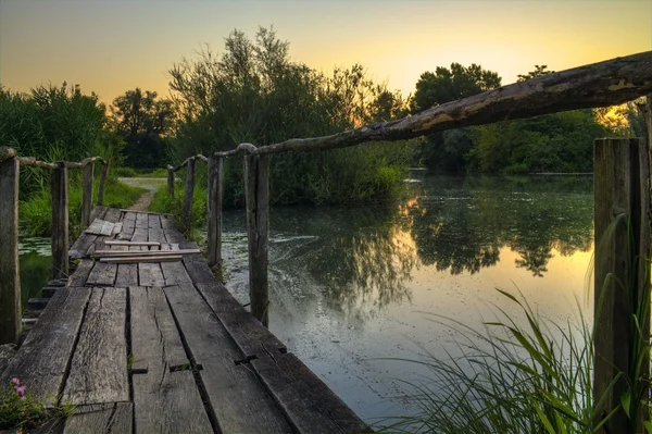 Puente de madera en un lago al amanecer — Foto de Stock