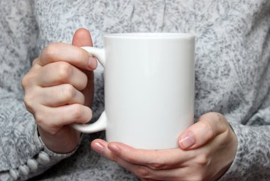 Girl is holding white cup in hands. White mug in woman's hands.