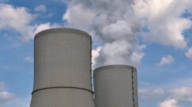 Bulutlu bir gökyüzüne karşı buharı tüten iki enerji santrali.