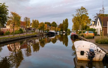 IJLST, NETHERLANDS - SEP 29, 2017: Geeuw canal with boats and houses in golden hour, city of IJlst, Friesland