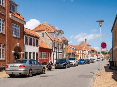 Kerteminde, Danimarka - 5 Ağustos 2025: Langegade boyunca park halindeki arabalar ve çatıların üzerinde yükselen tuğla bacalı evler, Funen, Güney Danimarka