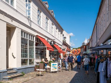 Ebeltoft, Danimarka - 9 Ağustos 2025: Eski Ebeltoft, Jutland, Danimarka 'daki Adelgade parke sokağında gezinen ve alışveriş yapan insanlarla dolu bir kafeterya