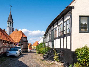 Ebeltoft, Danimarka - 9 Ağustos 2025: Yarı keresteli evler ve tarihi Ebeltoft, Jutland, Danimarka 'daki tarihi belediye binası ile Torvet' e doğru sokak manzarası Overgade