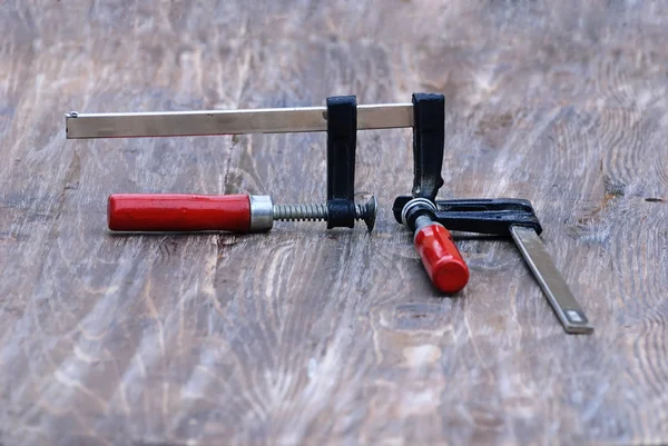 Two clamps tightly compressed together located on the wooden top — Stock Photo, Image