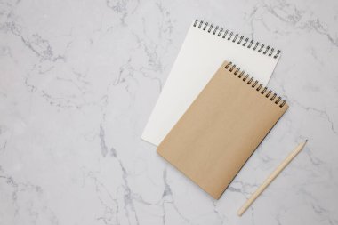 Mermer masa üzerinde kalem olan iki boş not defteri.