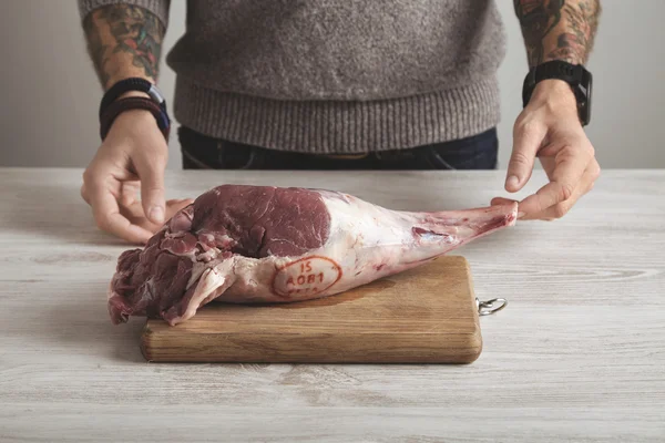 Tetovált hentes nyers bárány-láb tartja kezében — Stock Fotó