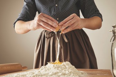 Woman breaks egg above flour clipart