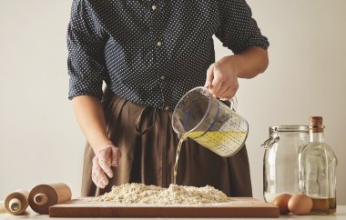 Woman pours water with olive oil to dough clipart