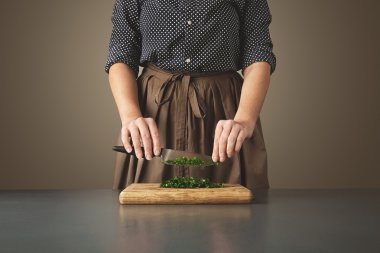 Woman holds knife above chopped green parsley clipart