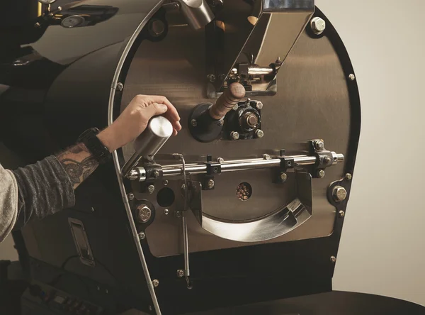 Getatoeëerde hand trekt hefboom in koffiebranderij machine — Stockfoto