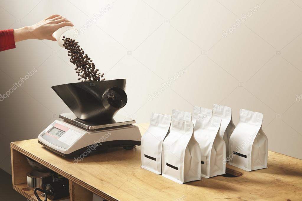 Hand pours roasted coffee on weight before package bag