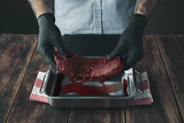 Carniceiro tatuado segura pedaço de carne acima do corante de aço — Fotografia de Stock