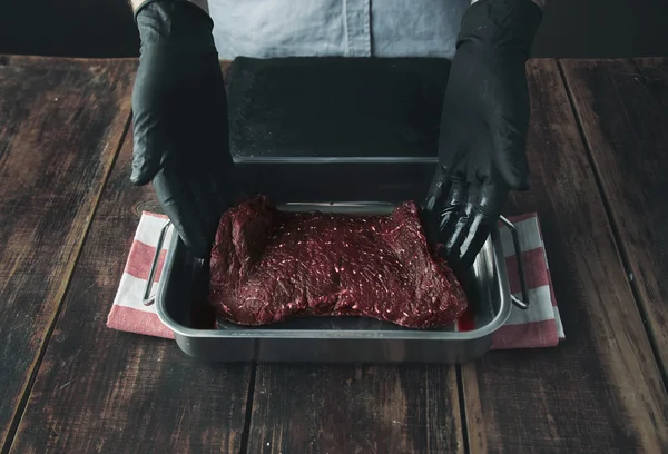 Татуйований м'ясник пропонує шматок сирого м'яса в сталевому штабелі — стокове фото