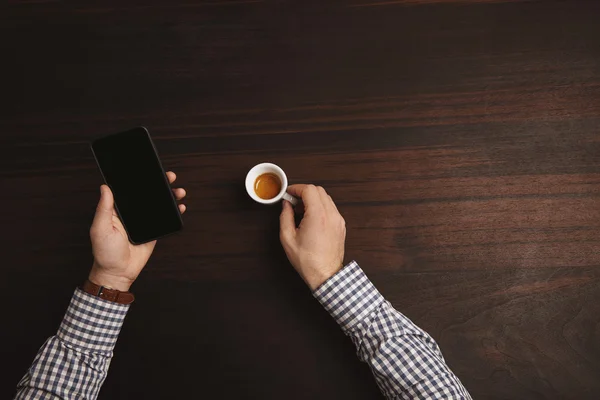 Empresario manos viendo el teléfono inteligente y mantenga espresso — Foto de Stock