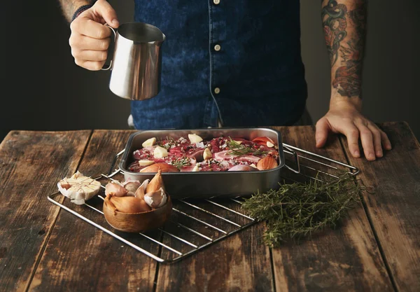 Boucher avec les mains tatouées tient le pot de sauce en acier au-dessus du colorant métallique — Photo